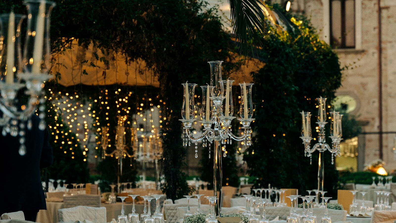 A long candlelit wedding table set with greenery in an English garden at dusk