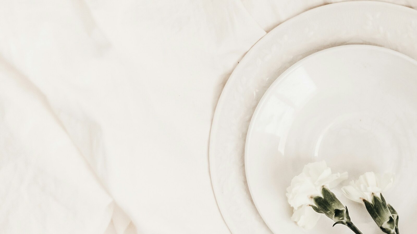 A calm wedding table setting in neutral linen with greenery